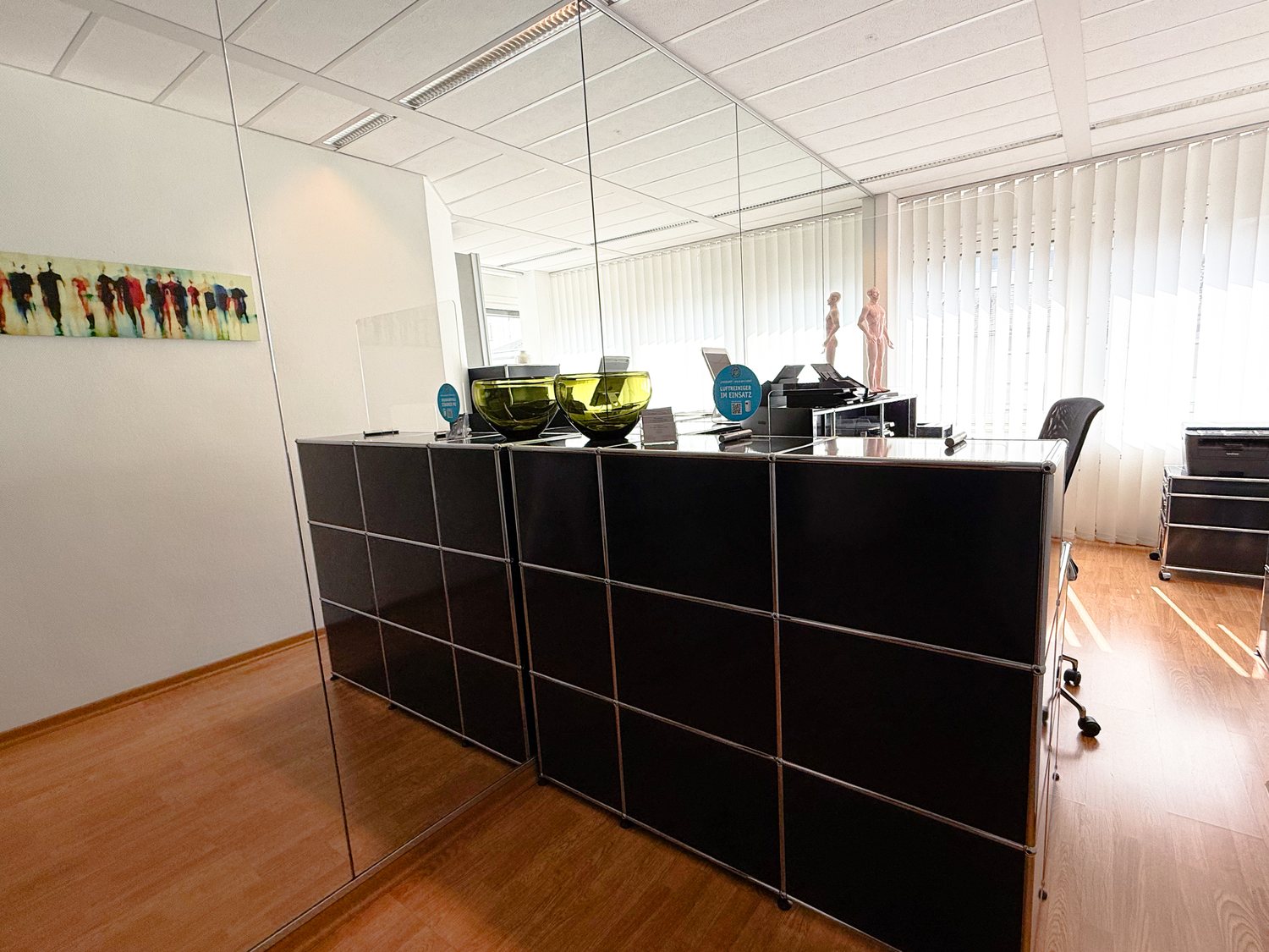 Anmeldung der Praxis mit dunklem Tresen, Spiegelwand und Blick in den Anmeldebereich